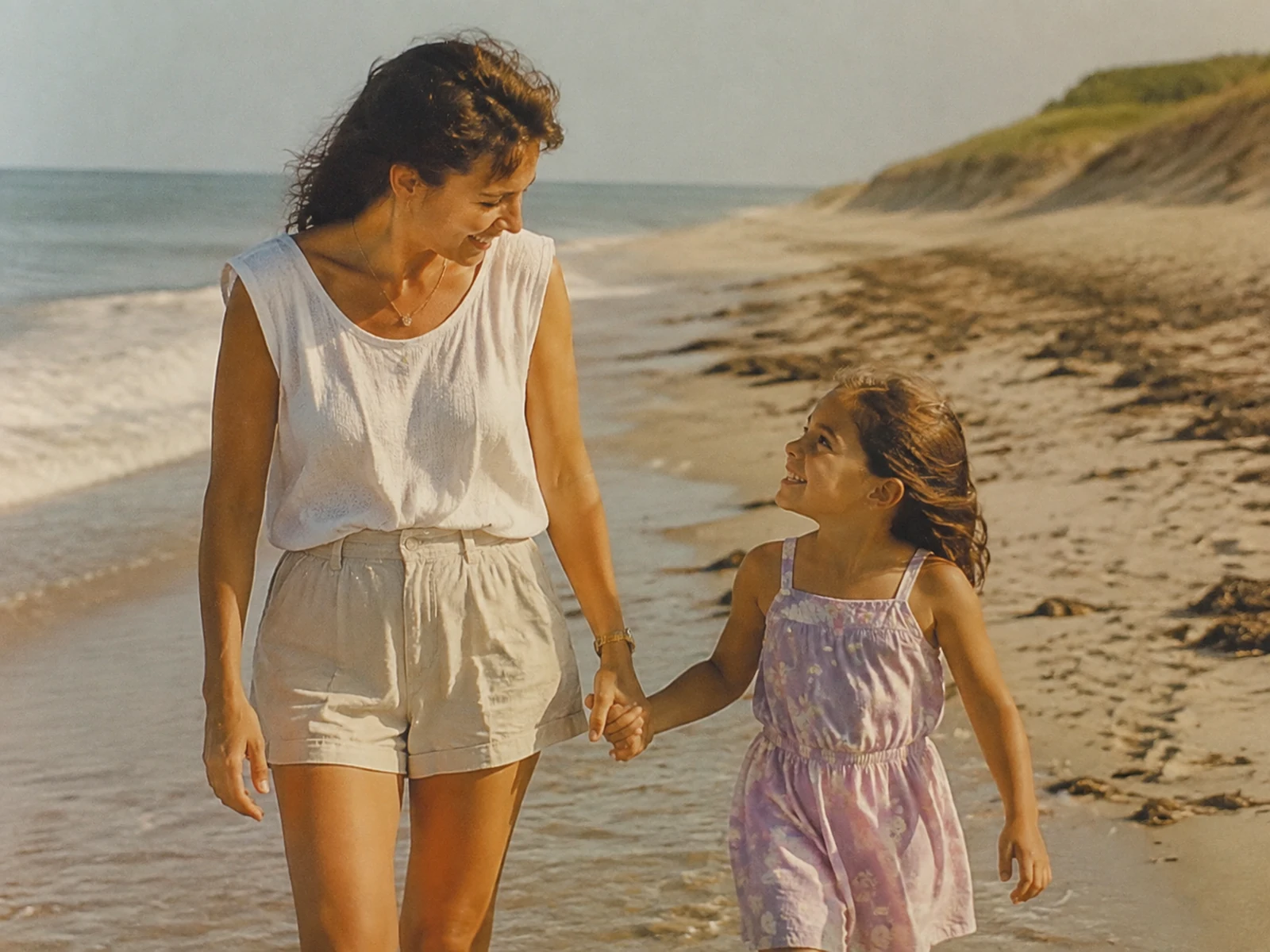 Una madre y su hija pequeña caminan de la mano por la playa